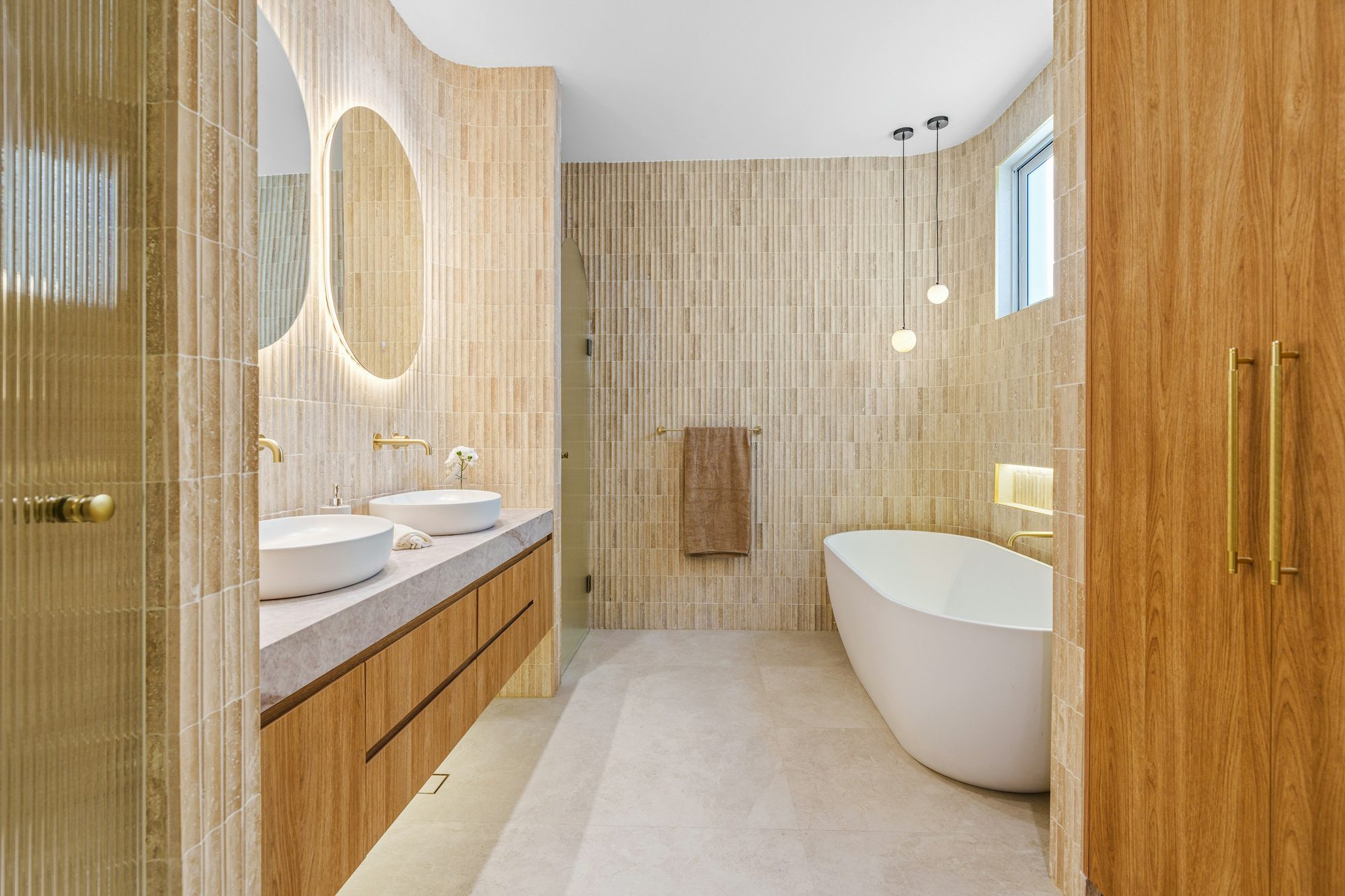 Bagno rifinito con doppio lavabo, vasca e rivestimenti in legno chiaro